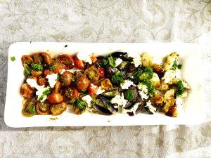 Grilled vegetable salad with cherry tomatoes, artichokes, red onions, mozzarella and parsley oil on a white serving plate