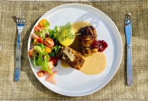 Finnish cabbage rolls (Kaalikääryleet) on a rustic plate with lingonberry jam, boiled potato with dill, creamy sauce, and fresh salad.