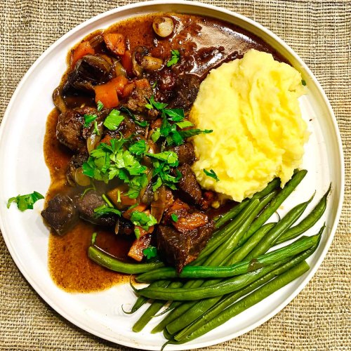Beef Bourguignon with red wine sauce, served with creamy mashed potatoes and steamed green beans, garnished with fresh parsley.