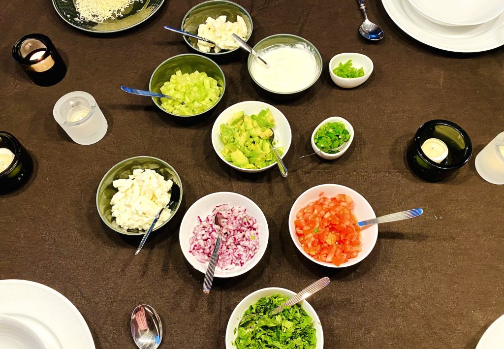 Chili Toppings in Small Bowls – Fresh and Colorful Small bowls filled with chili toppings including tomato, avocado, sour cream, cilantro, serrano slices, mozzarella, grated Emmental, red onion, and chopped cucumber