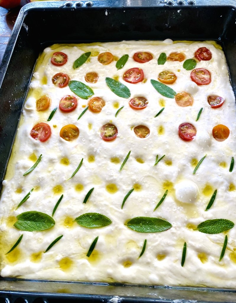 Sourdough focaccia dough topped with cherry tomatoes, rosemary, and sage before baking