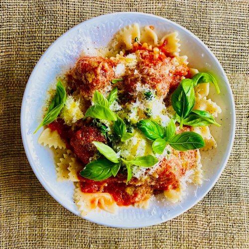 Italian meatballs with tomato sauce, fresh basil, and grated Parmesan served with pasta in a white bowl.