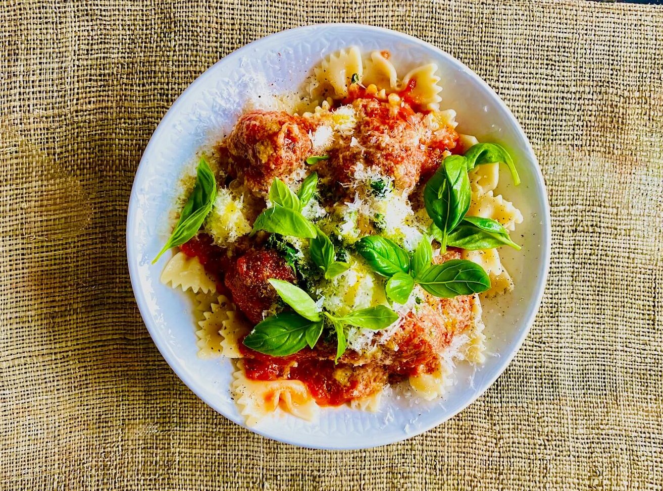 Italian meatballs with tomato sauce, fresh basil, and grated Parmesan served with pasta in a white bowl.