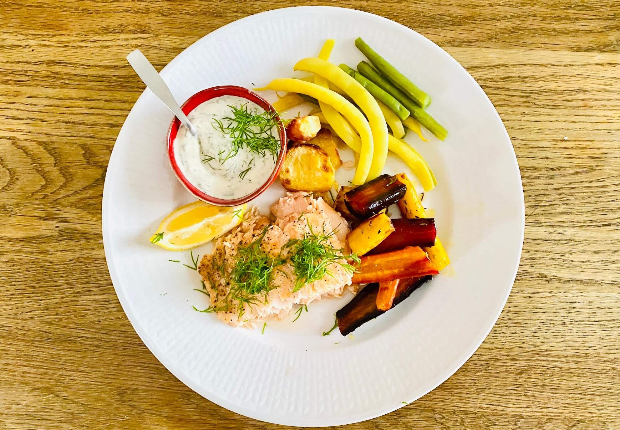 Oven-baked salmon fillet with dill and Finnish kermaviili sauce, served with roasted carrots and sliced potatoes.