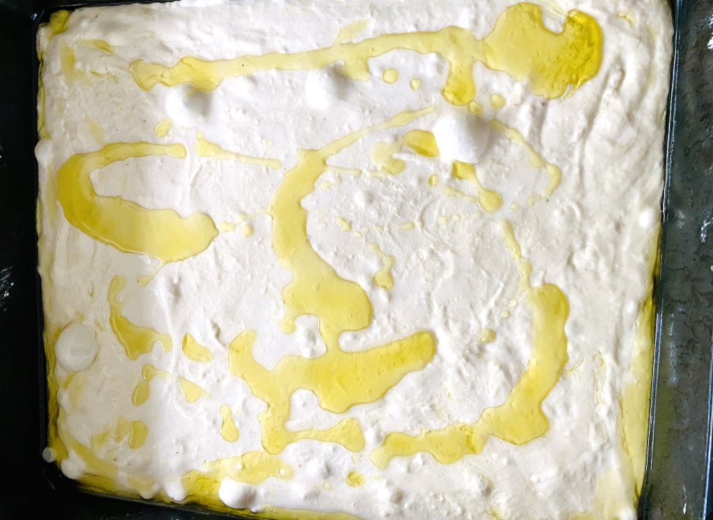 Sourdough focaccia dough stretched in an oiled pan with visible air bubbles.