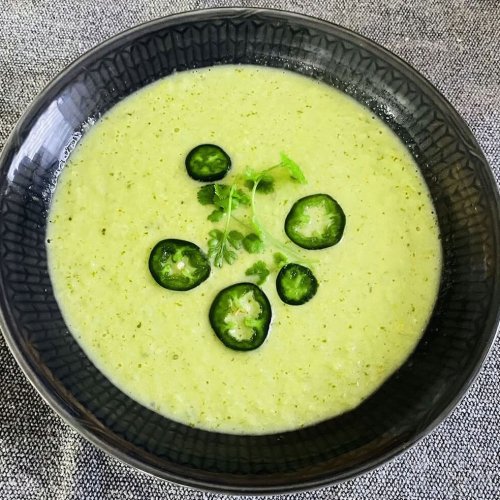 A bowl of creamy tomatillo soup topped with fresh cilantro leaves and thin jalapeño slices.