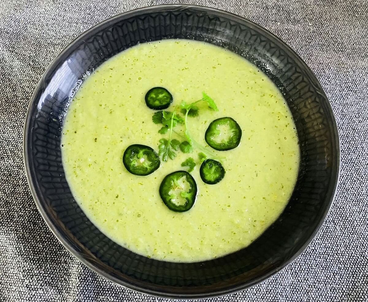A bowl of creamy tomatillo soup topped with fresh cilantro leaves and thin jalapeño slices.