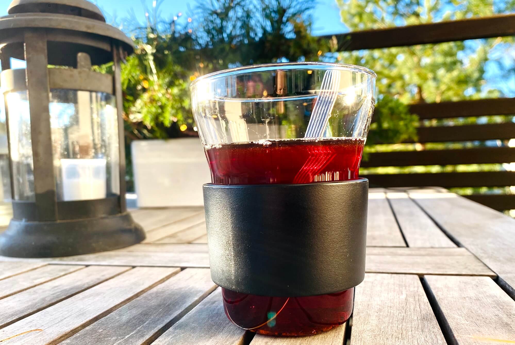 A glass of red glögi on a wooden outdoor table in bright sunlight.