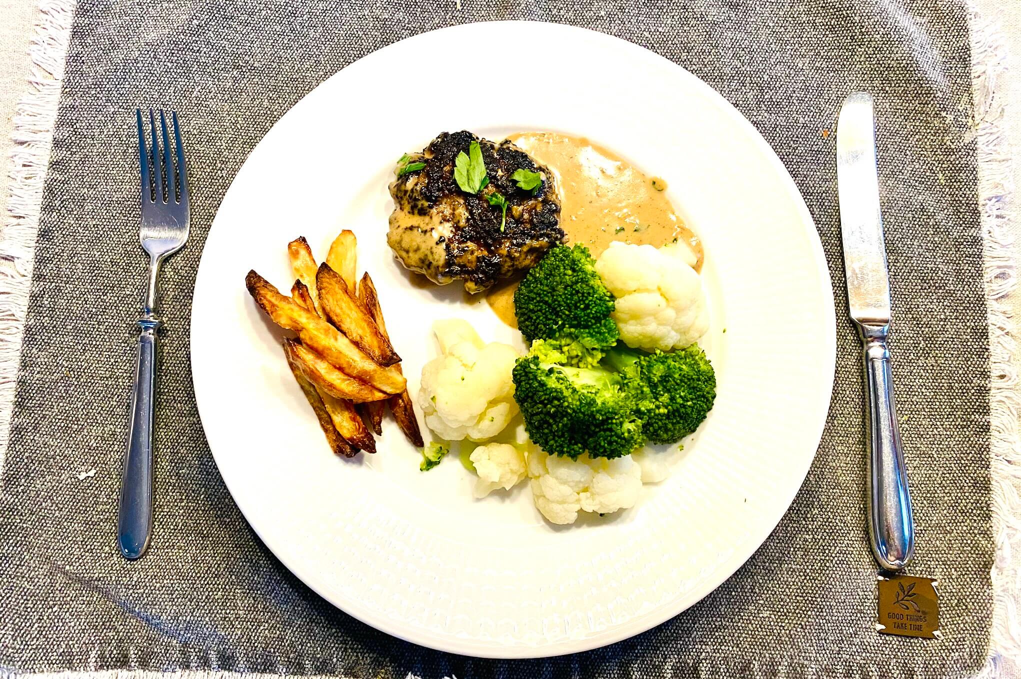 Plate with Finnish ground beef patty in mustard cream sauce, homemade fries, steamed broccoli and cauliflower.