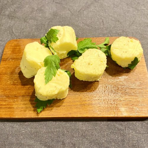 Slices of truffle butter are arranged on a small wooden board, topped with parsley leaves.