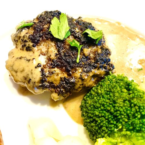 Close-up of Finnish ground beef patty in creamy mustard sauce, served with a few vegetable sides.