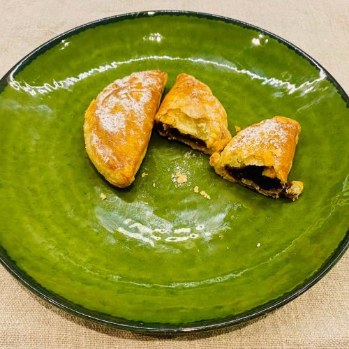 Two Finnish joulutortut on a green plate, one whole and one halved to reveal the tender pastry and smooth plum filling inside.