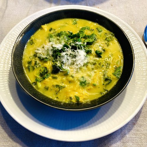 Chicken soup with ginger, lemon, broccoli, and pasta in a bowl, garnished with parsley and grated Parmesan