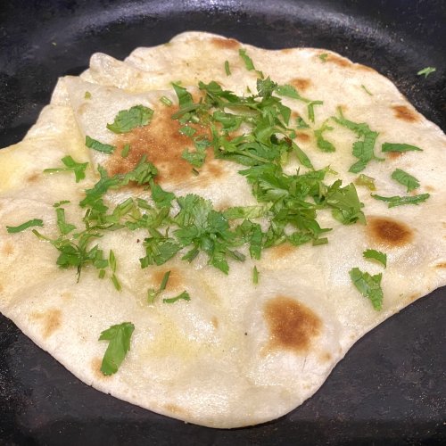 Flatbread cooking in a skillet, brushed with garlic butter and topped with fresh herbs.