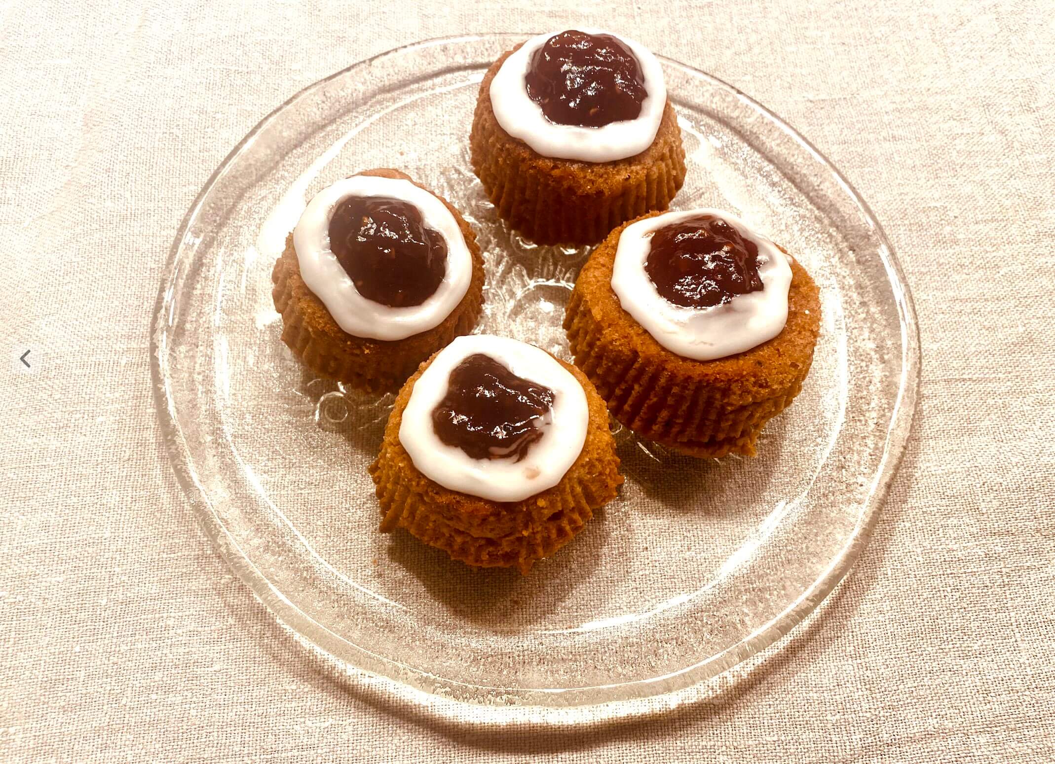 Several rustic Runeberg tortes (Runebergintorttu) on a clear glass plate, topped with raspberry jam and icing