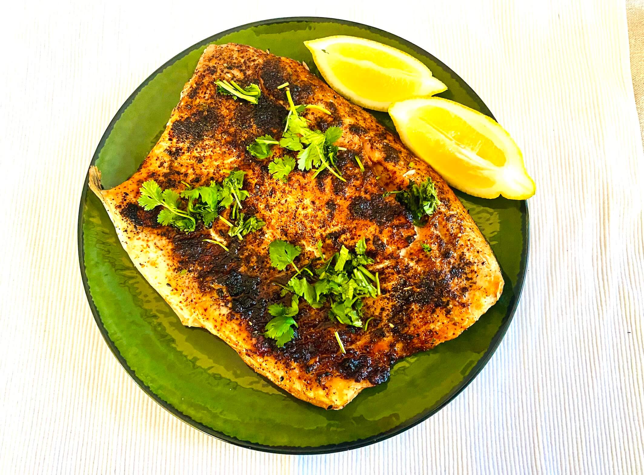 Air fryer roasted salmon fillet garnished with fresh cilantro and lemon wedges on a serving plate