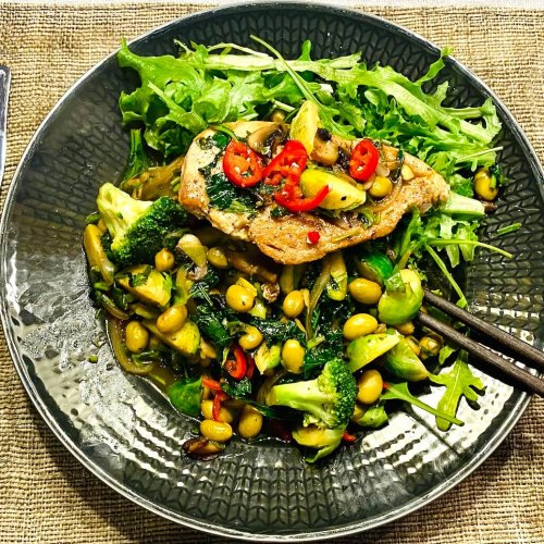 Asian chicken salad with pan-fried chicken, warm vegetables, arugula, edamame beans, fresh red chili, and cilantro, served with a soy–sesame sauce.