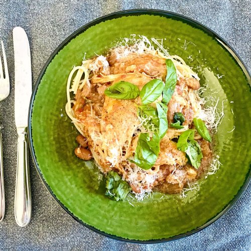 Chicken with Olives and Borlotti Beans served over spaghetti, topped with grated Parmesan and fresh basil, on a rustic green plate.