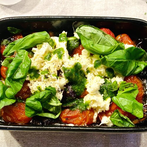 Roasted cherry tomatoes with basil oil and mozzarella in an oven dish, ready to serve