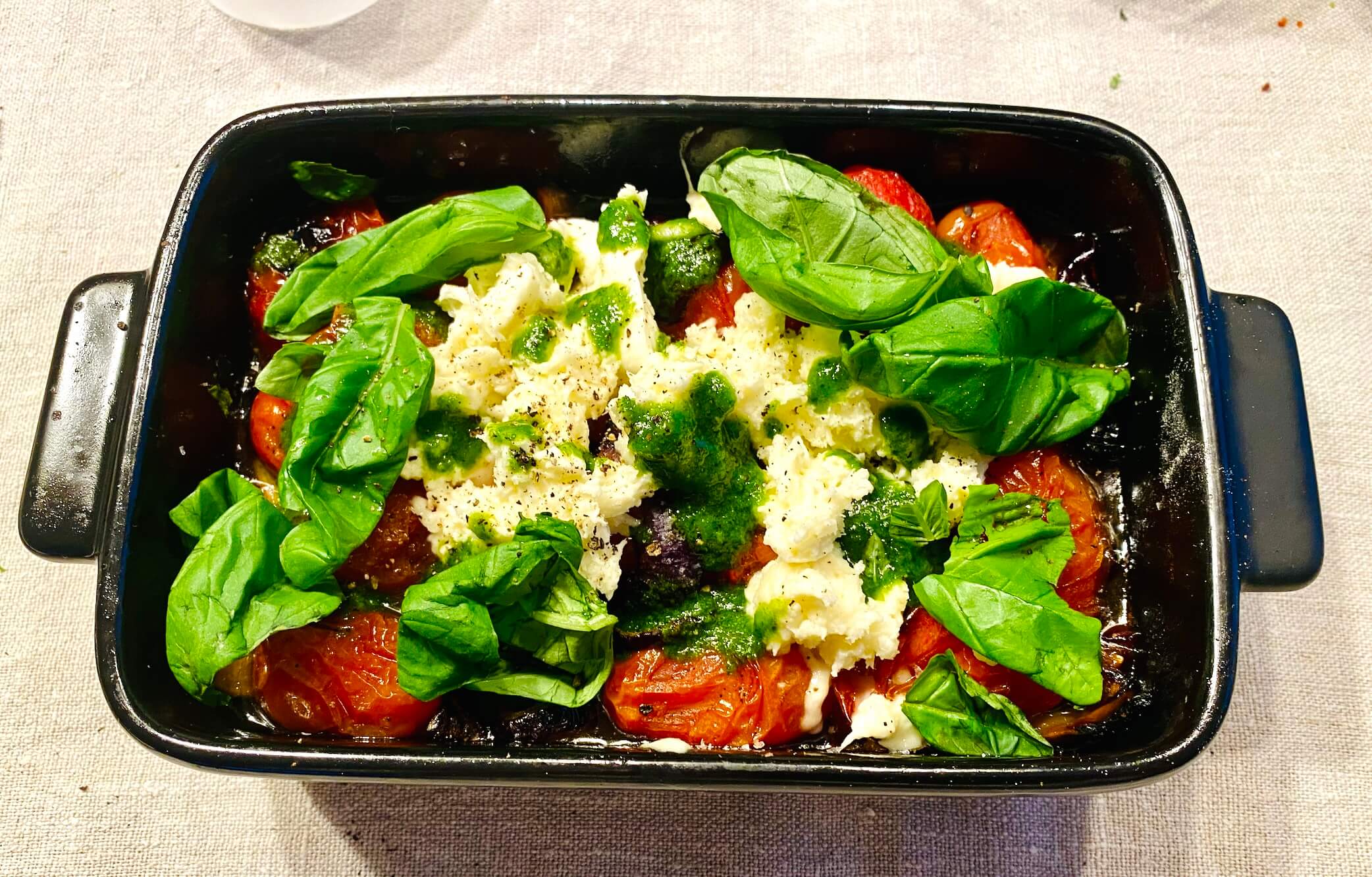 Roasted cherry tomatoes with basil oil and mozzarella in an oven dish, ready to serve
