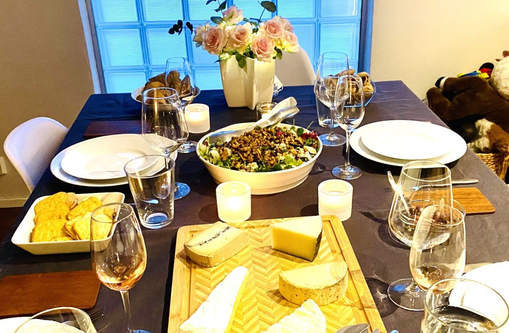 Evening table setting with Blue Cheese Grape Salad, cheeses, glasses of sparkling wine, candles, and flowers.