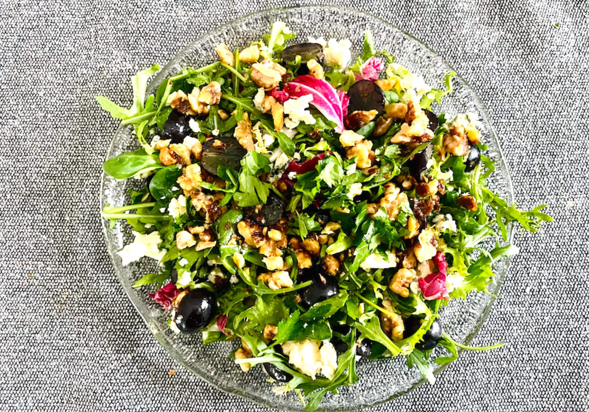 Blue cheese grape salad with mixed greens and caramelized walnuts in a glass bowl