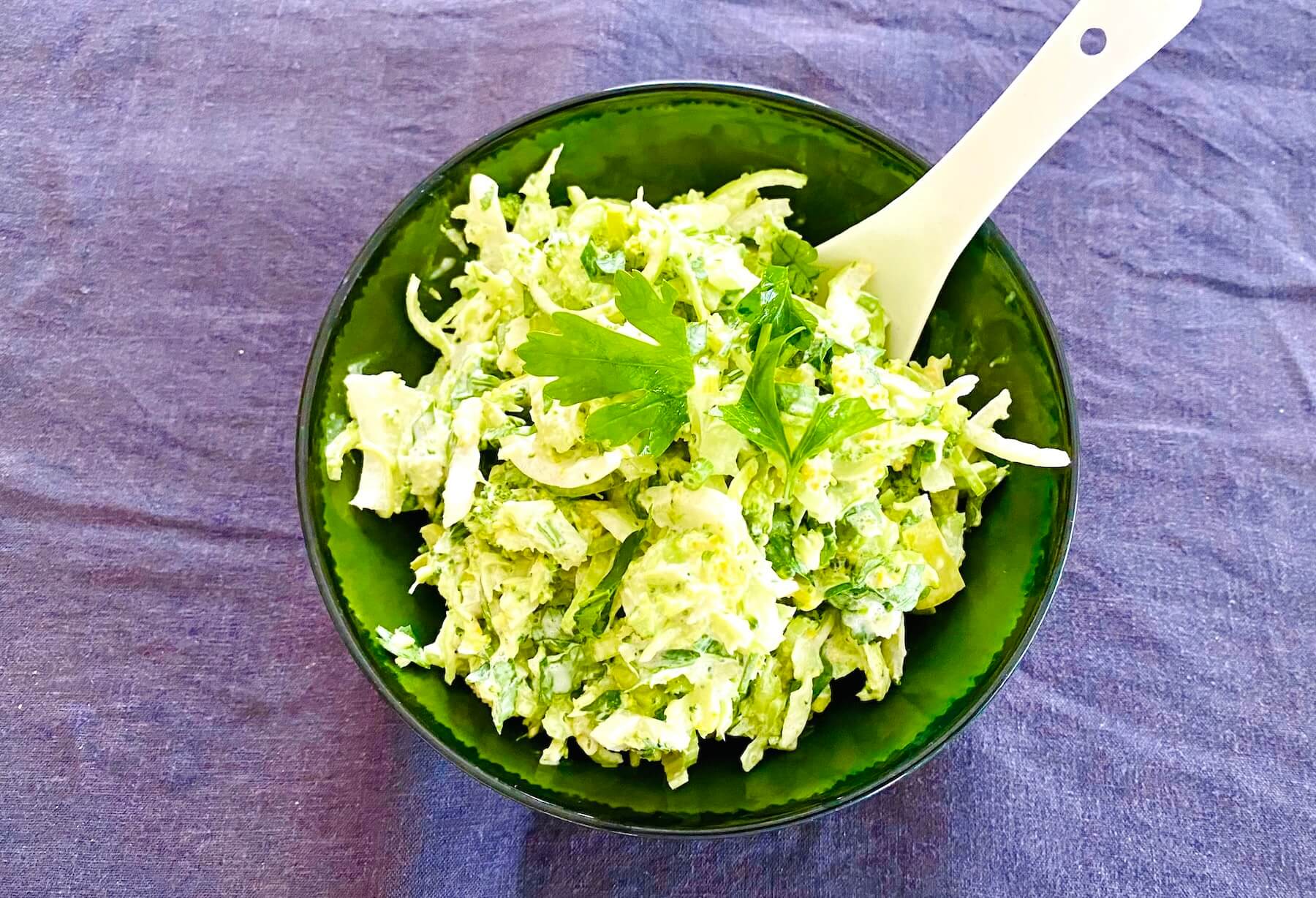 Broccoli slaw with crème fraîche dressing served in a rustic dark green bowl.