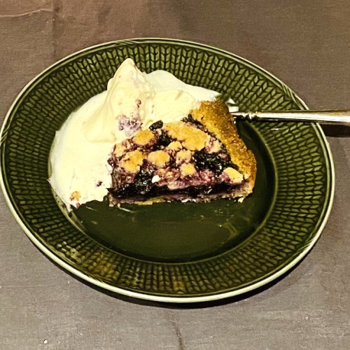 Slice of gluten-free blueberry pie with almond flour crust served on a plate with vanilla ice cream.