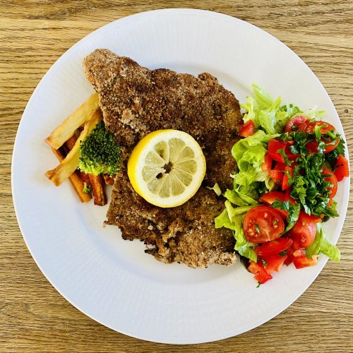 Pork Wiener schnitzel with lemon slice, tomato salad, carrot and potato fries, and broccoli