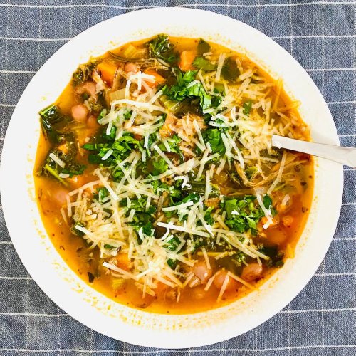Bean and kale soup served in a white soup plate, topped with parsley and grated Parmesan.