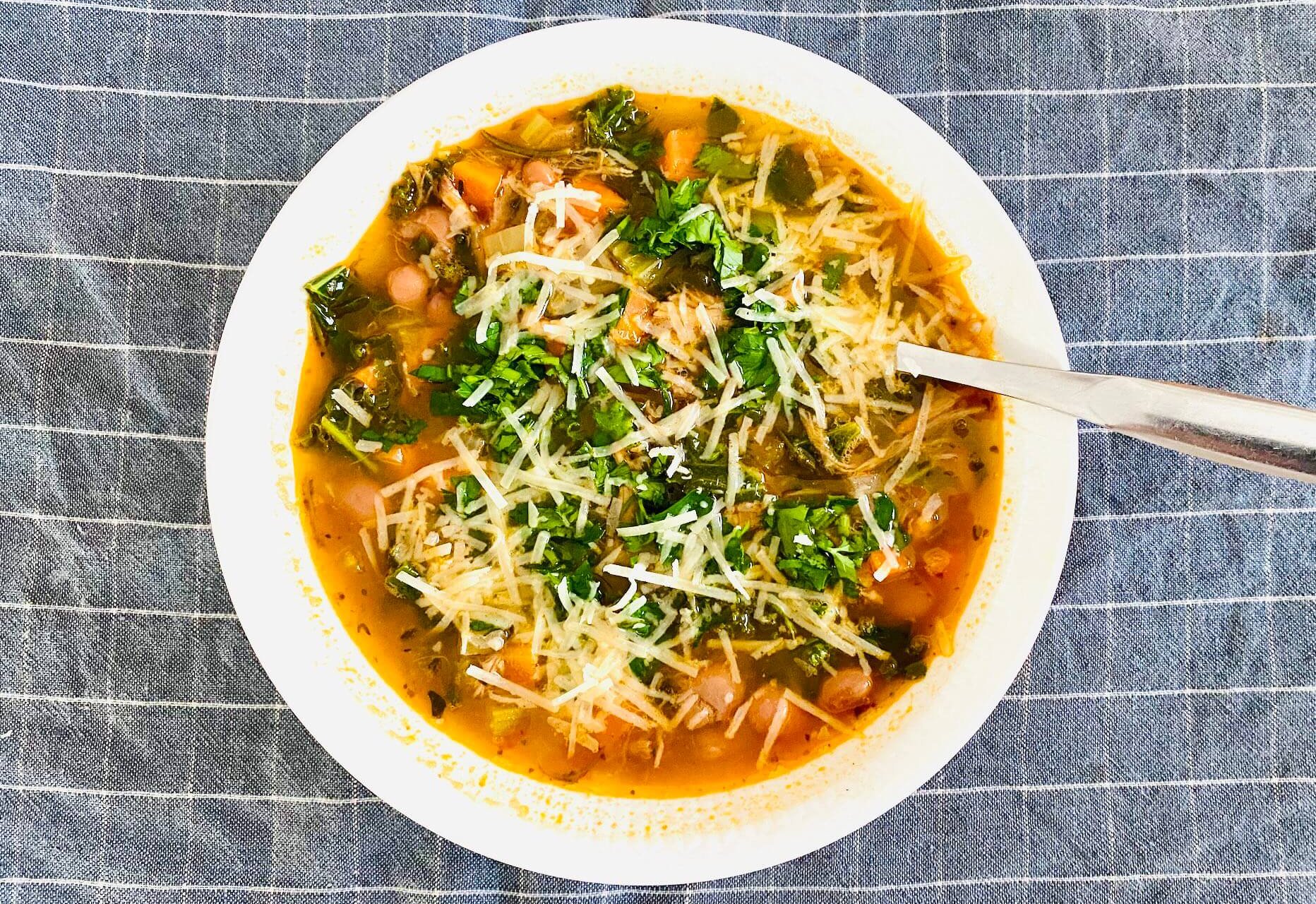 Bean and kale soup served in a white soup plate, topped with parsley and grated Parmesan.