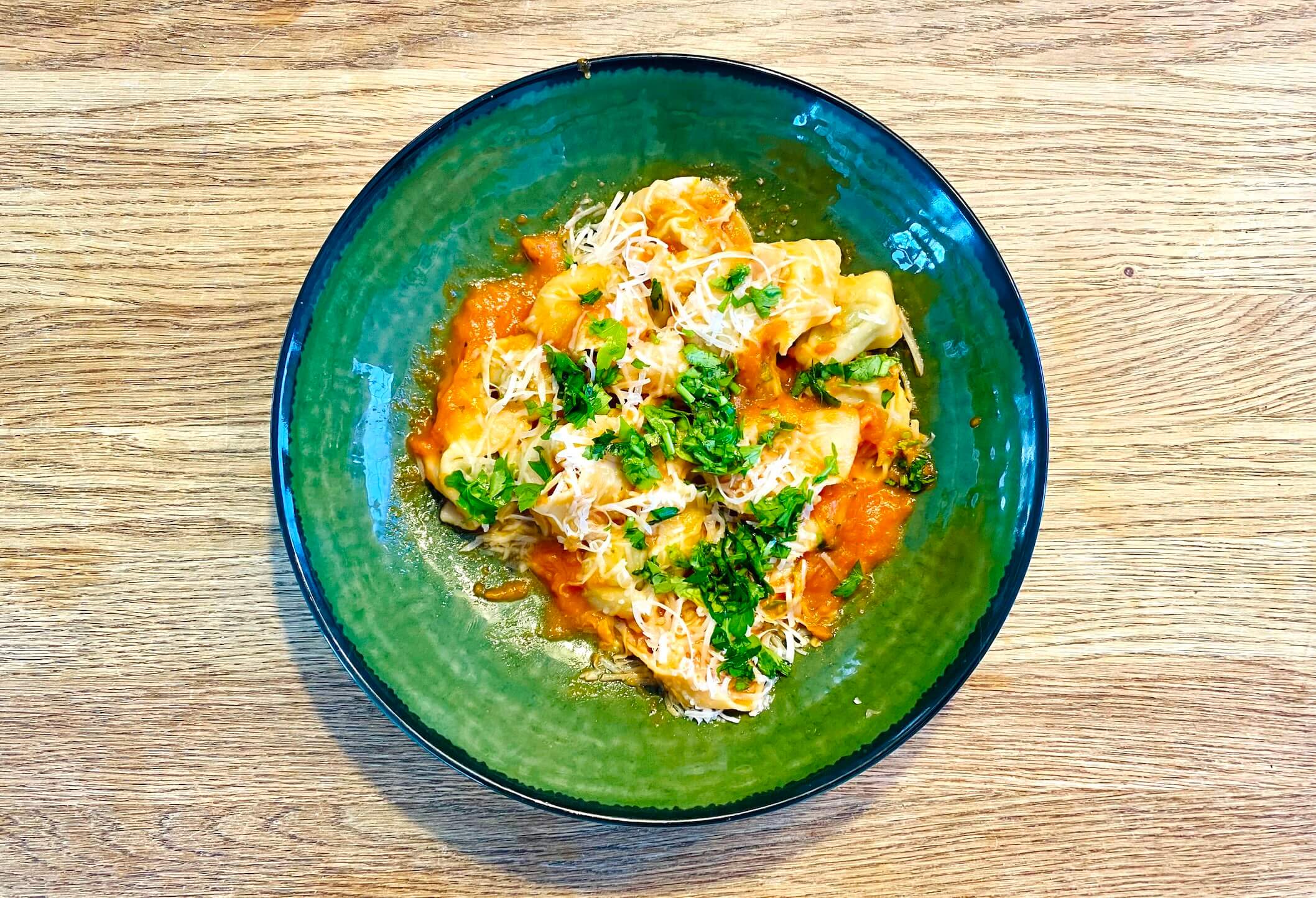Ricotta spinach tortellini in tomato sauce garnished with fresh herbs, on a plate