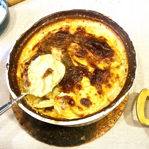 Finnish creamy garlic potatoes (Valkosipuliperunat) in a white ceramic baking dish with golden browned top and creamy layers served on a spoon