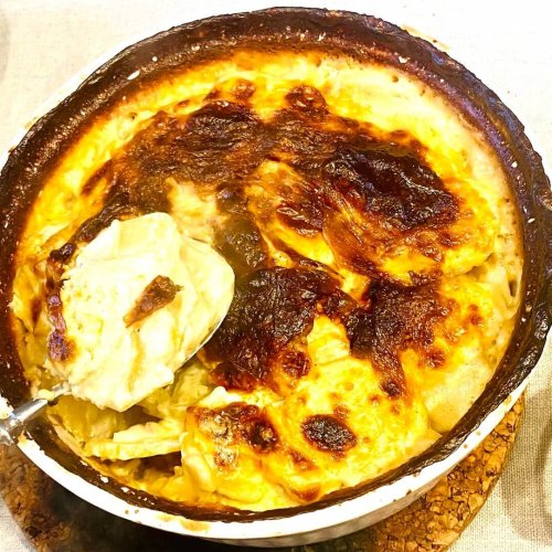 Finnish creamy garlic potatoes (Valkosipuliperunat) in a white ceramic baking dish with golden browned top and creamy layers served on a spoon