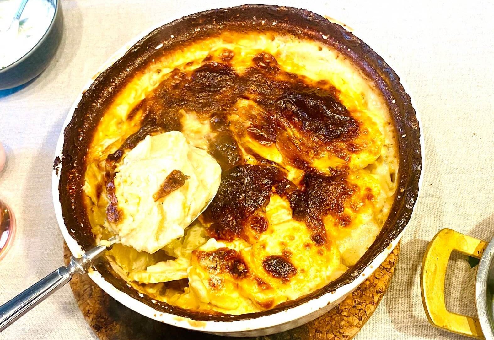 Finnish creamy garlic potatoes (Valkosipuliperunat) in a white ceramic baking dish with golden browned top and creamy layers served on a spoon