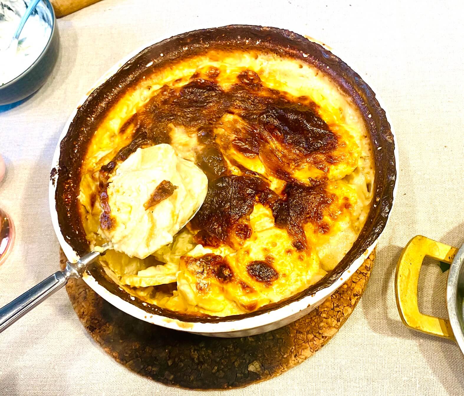Finnish creamy garlic potatoes (Valkosipuliperunat) in a white ceramic baking dish with golden browned top and creamy layers served on a spoon
