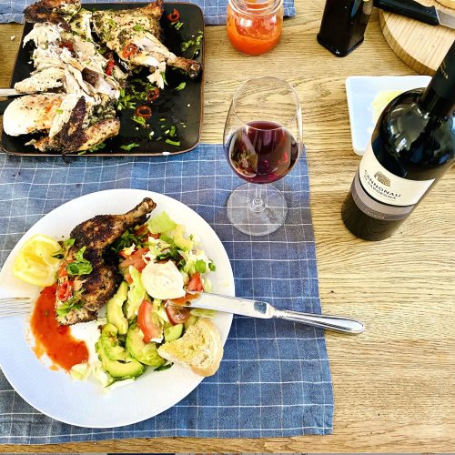 Grilled spatchcock chicken served with salad, rustic bread dipped in olive oil, homemade hot sauce, and red wine on a table setting