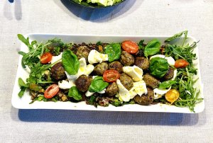 Warm meatball and mozzarella salad with beluga lentils, fresh greens, and cherry tomatoes on a serving plate