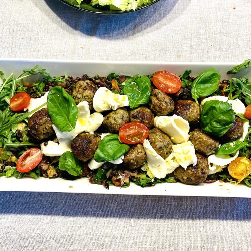 Warm meatball and mozzarella salad with beluga lentils, fresh greens, and cherry tomatoes on a serving plate