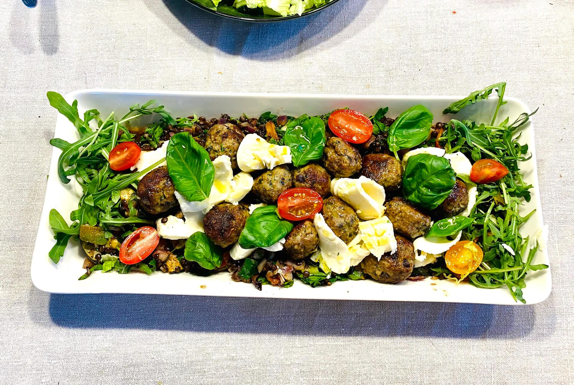 Warm meatball and mozzarella salad with beluga lentils, fresh greens, and cherry tomatoes on a serving plate