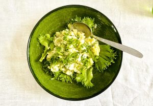 Creamy Finnish potato salad with capers, pickled cucumber, and parsley served in a green bowl on lettuce leaves