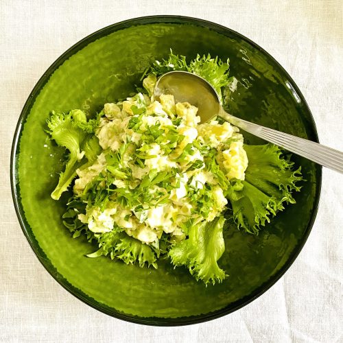 Creamy Finnish potato salad with capers, pickled cucumber, and parsley served in a green bowl on lettuce leaves