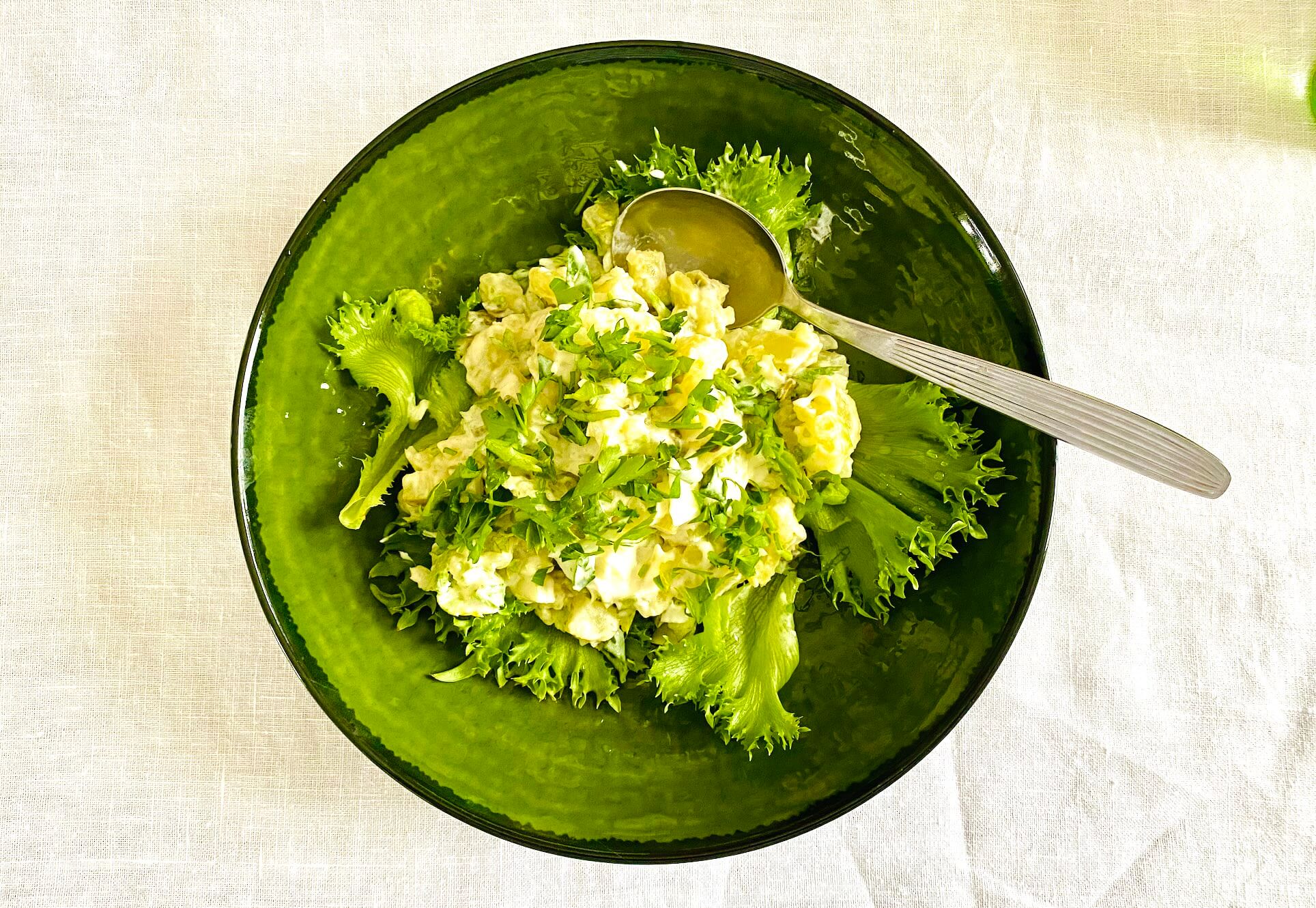 Creamy Finnish potato salad with capers, pickled cucumber, and parsley served in a green bowl on lettuce leaves