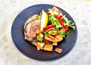 Pork loin steaks with Dijon cream sauce served with roasted root vegetables and fresh green salad on a dark gray plate