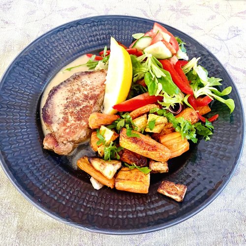 Pork loin steaks with Dijon cream sauce served with roasted root vegetables and fresh green salad on a dark gray plate