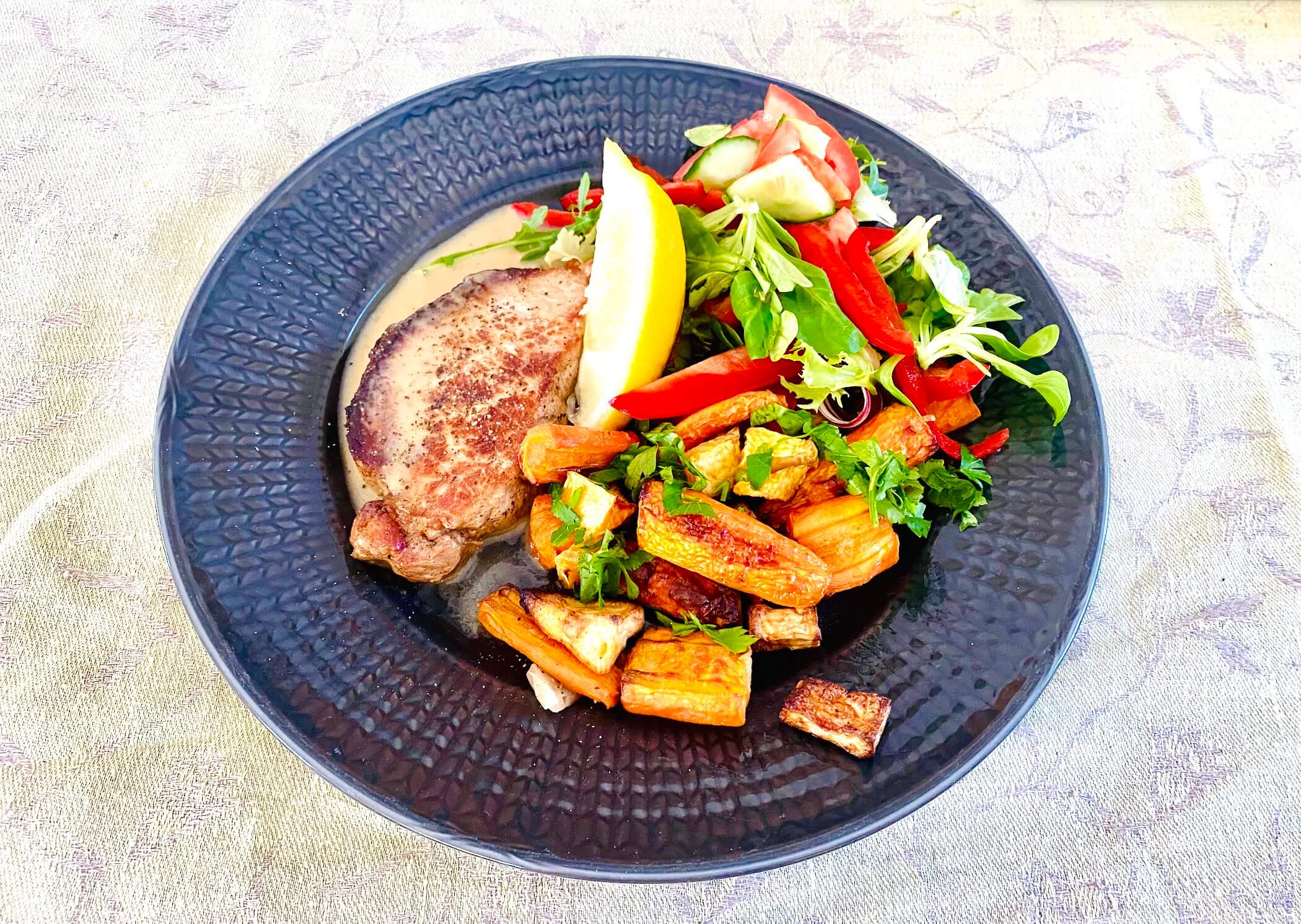 Pork loin steaks with Dijon cream sauce served with roasted root vegetables and fresh green salad on a dark gray plate