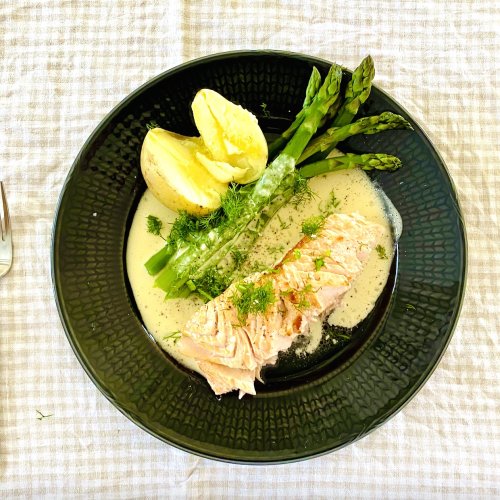 Oven baked salmon with creamy dill white wine sauce, green asparagus, and buttery Finnish new potatoes on a dinner plate