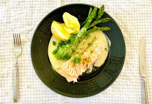 Oven baked salmon with creamy dill white wine sauce, green asparagus, and buttery Finnish new potatoes on a dinner plate