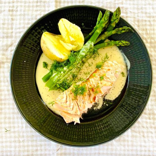 Oven baked salmon with creamy dill white wine sauce, green asparagus, and buttery Finnish new potatoes on a dinner plate