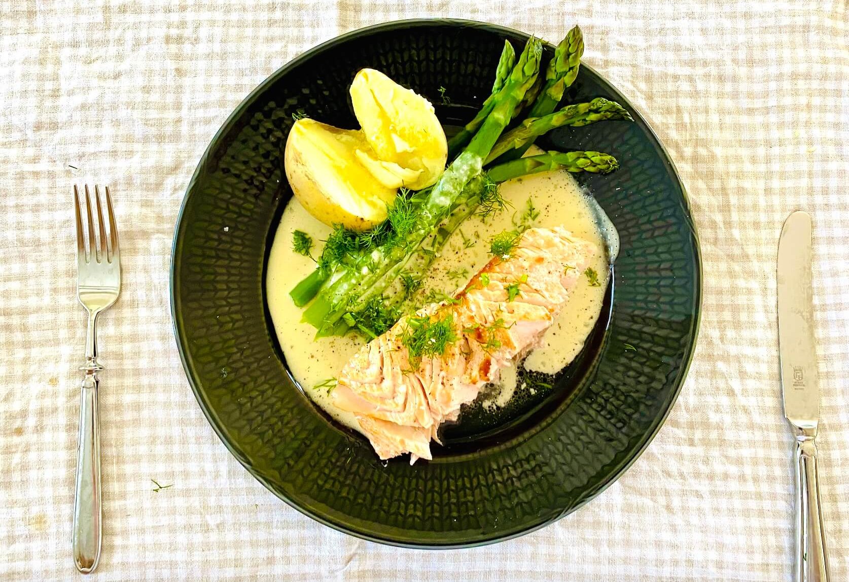 Oven baked salmon with creamy dill white wine sauce, green asparagus, and buttery Finnish new potatoes on a dinner plate